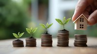 Growing stacks of coins with green plant sprouts and small wooden house, representing financial growth, investment and sustainable development concept.