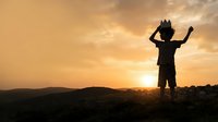 Silhouette of child with raised arms celebrating against golden sunset sky with mountains in background, representing joy, freedom, and achievement for motivational and inspirational content.