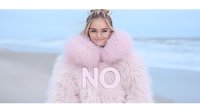 Young blonde woman in pink fluffy faux fur coat with NO text on beach, wearing glasses and messy bun hairstyle against blurred ocean background.
