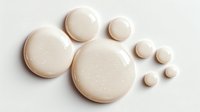 Creamy beige liquid foundation drops or concealer samples on white background, isolated for beauty product advertising.