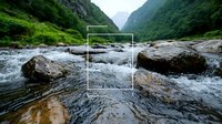 Mountain stream flowing through rocky terrain with rushing water cascading over boulders in dramatic valley landscape. Green slopes and misty peaks frame wilderness scene.