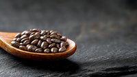 Fresh roasted coffee beans on wooden spoon against dark stone background, dramatic lighting creates mood for coffee shop menu or blog post.