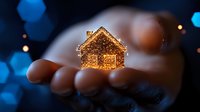 Glowing miniature house resting in open palm against dark background with blue bokeh lights creates magical atmosphere for real estate and holiday concepts.