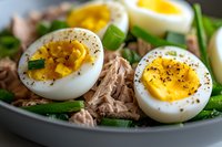 Fresh tuna salad with halved boiled eggs, mixed greens and black pepper seasoning in bowl. Healthy protein-rich meal for diet and fitness nutrition.