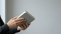 Senior man with wrinkled hands holding an open book against neutral background, suitable for education, literacy, reading, and learning concepts.