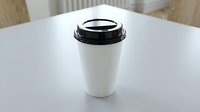 White disposable coffee cup with black lid on table in modern cafe interior for takeaway beverage service and restaurant branding mockup.