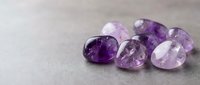Purple amethyst gemstones in various shades scattered on neutral surface for jewelry making, crystal healing, and luxury accessories design projects.