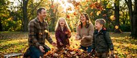 Family of four enjoying autumn outdoors, playing in fallen leaves during golden hour in forest setting. Parents and two children bonding together.