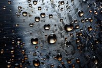 Clear water drops on dark surface with dramatic lighting create abstract pattern. Golden reflections in spherical droplets against black background add depth and texture.