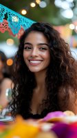 Young Latin woman with curly dark hair and bright smile at outdoor party with festive papel picado decorations and bokeh lights in background.
