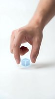 Male hand reaching to pick up a glowing blue transparent cube on white background, symbolizing technology, data, and digital innovation.