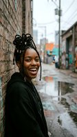 Happy young African American woman with braided hair laughing joyfully on urban street with brick wall and colorful graffiti background.