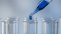 Laboratory pipette dropping blue liquid into test tubes for scientific research and chemical analysis experiments.