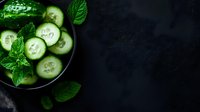 Fresh cucumber slices with vibrant mint leaves in dark bowl against black background, moody food photography composition with copy space for menu design.