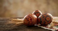 Traditional decorated Easter eggs with intricate folk patterns on rustic wooden surface with wheat stalks creating warm holiday atmosphere.