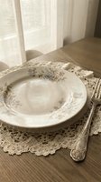 Vintage floral porcelain plate with ornate silverware on lace doily, sunlit dining setup for elegant table settings and formal dining concepts.