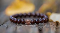 Dark brown wooden beaded bracelet with ornate copper accent bead on rustic wooden surface, soft natural lighting creates gentle bokeh effect in background.