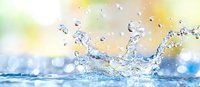 Clear water splash with droplets creating dynamic crown shape against soft yellow and green bokeh background, fresh motion capture with sparkling effect.