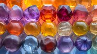 Colorful glass gems backlit with bright light creating vibrant translucent pattern of purple, orange, yellow and red hexagonal shapes in rows for decorative design.