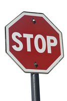 Red and white octagonal stop sign mounted on metal pole against neutral background, isolated view showing clear text and mounting hardware.