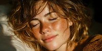 Young woman with freckles and tousled blonde hair enjoying warm sunlight with eyes closed in peaceful moment of relaxation and natural beauty.