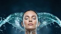 Young woman with closed eyes surrounded by dynamic water splash against dark background for skincare and beauty advertising campaigns.