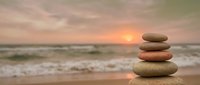 Zen stone stack on beach at sunset with ocean waves and golden sky creating peaceful meditation atmosphere for wellness and mindfulness practices.