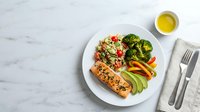 Healthy balanced meal with grilled salmon, quinoa salad, steamed vegetables and avocado on white plate. Nutritious dinner concept for clean eating lifestyle.