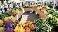 Farmers market with fresh produce displays including colorful vegetables and fruits, shoppers browsing stalls in sunny outdoor setting for retail, agriculture, food business.