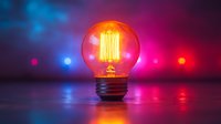 Glowing vintage light bulb with warm orange filament against vibrant blue and pink bokeh background creating atmospheric mood lighting effect.