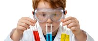 Young Caucasian girl scientist wearing safety goggles conducting chemistry experiment with colorful test tubes in laboratory setting for STEM education.