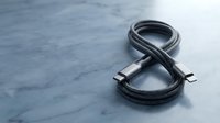 Black braided USB-C cable coiled in figure eight shape on marble surface. High-quality charging cord for smartphones, tablets and electronic devices.