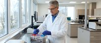 Middle-aged Caucasian male scientist in white lab coat and blue gloves conducting research with test tubes in modern laboratory setting for medical studies.