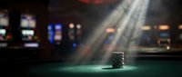 Stack of poker chips illuminated by dramatic spotlight on green felt casino table with blurred gaming machines and colorful lights in background.