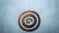 Coffee beans arranged in spiral pattern on textured blue background creating circular design for cafe branding and beverage marketing materials.
