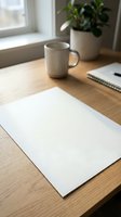 Blank white paper on wooden desk with ceramic mug, potted plant, notebook, and window in background. Mockup for branding, stationery design, and marketing materials.