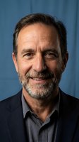 Professional mature Caucasian businessman with gray beard smiling confidently in dark suit against blue background for corporate headshot photography.
