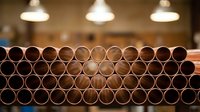 Industrial copper pipes stacked in rows at manufacturing facility with warm lighting creating depth of field effect for construction projects.