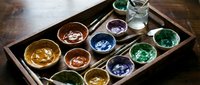 Watercolor paints in ceramic bowls arranged in wooden tray with brushes, artist supplies for painting and creative projects.