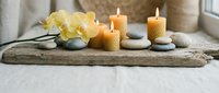 Spa wellness still life with burning beeswax candles, zen stones, and yellow orchid flowers on rustic driftwood for relaxation decor.