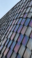 Modern building facade with iridescent metal panels arranged in overlapping geometric pattern, reflecting sky in blue and purple tones, contemporary architecture detail for design projects.