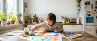 Young boy with brown hair painting colorful artwork at wooden table in bright kitchen, creative child engaged in art activity at home.