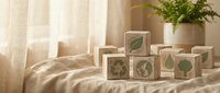 Wooden eco-friendly blocks with green leaf symbols arranged on natural linen fabric near window with soft sunlight and houseplant for sustainable living concept.