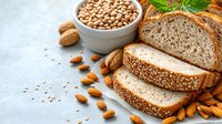 Fresh whole grain bread slices with raw almonds, chickpeas in ceramic bowl and walnuts on light blue background, healthy protein food sources.
