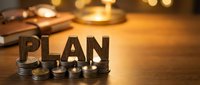 Financial planning concept with wooden PLAN letters on stacked coins beside calculator and pen on warm desk surface for business strategy development.