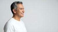 Mature Caucasian man with gray hair smiling confidently in white shirt against neutral background for business and lifestyle concepts.