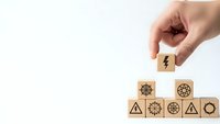 Hand placing wooden cube with lightning bolt symbol completing energy and power icon collection on white background for business concepts.
