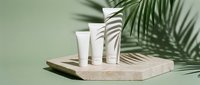 Cosmetic skincare products displayed on natural stone platform with tropical palm leaf shadows against soft green background.