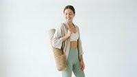 Young woman with East Asian ethnicity wearing casual sustainable fashion, holding woven tote bag with reusable water bottle. Eco-conscious lifestyle and zero waste shopping concept.