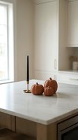 Minimalist autumn kitchen decor with orange pumpkins and black candle on marble countertop in modern neutral interior for seasonal home styling.